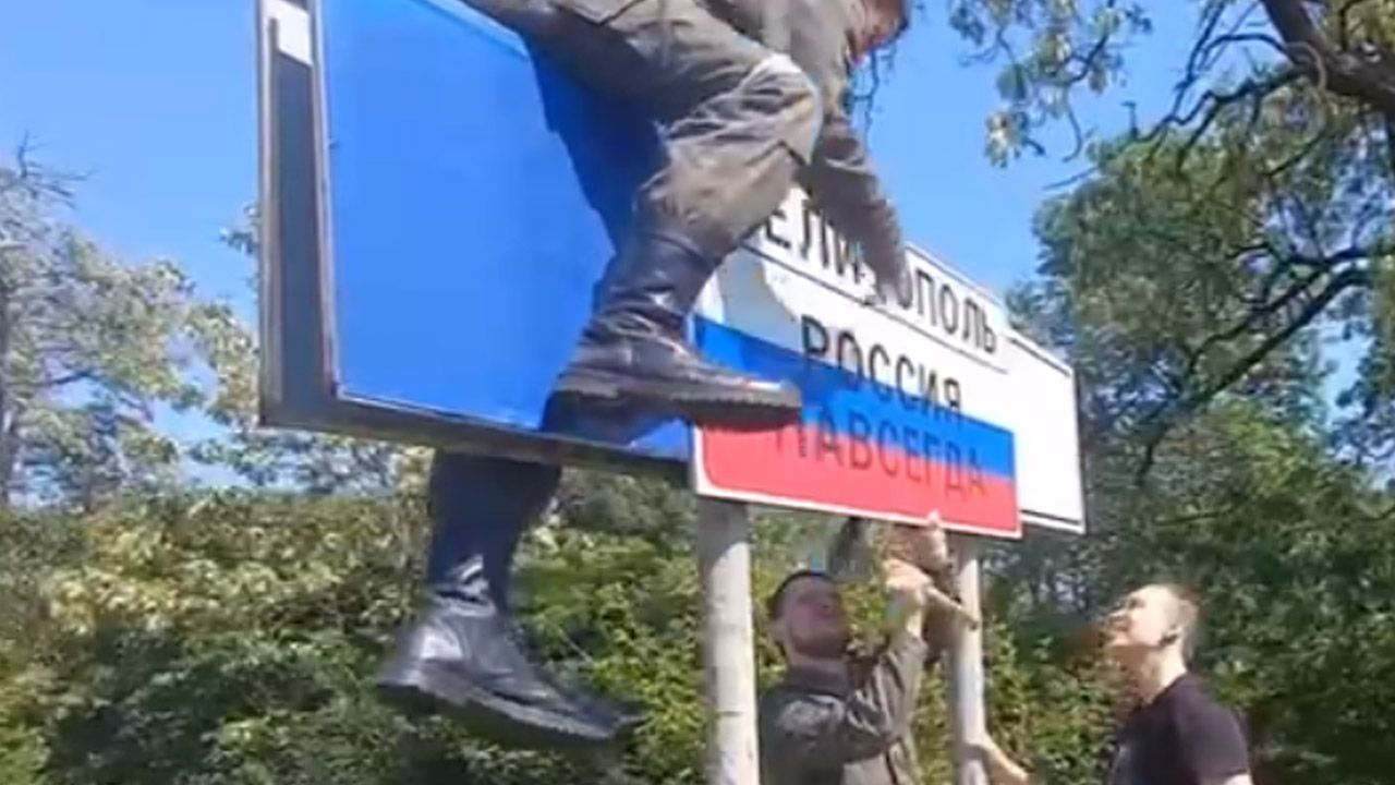 Rosjanie zawieszają tabliczkę na wjeździe do Melitopola (fot. Telegram/Букви. Війна. Україна)